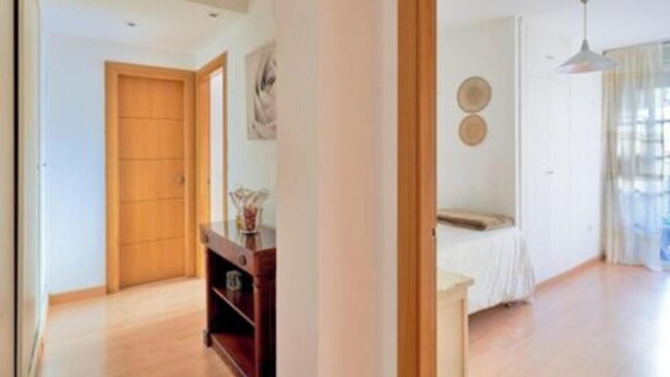 Una habitación con una cama, una puerta de madera, una mesita pequeña y un estante fijado a la pared.