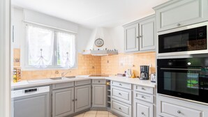 Eine Küche mit grauen Schränken, einem Geschirrspüler, einem Backofen und einem Fenster mit Vorhängen.