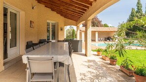 Eine Terrasse im Freien mit einem langen Tisch und Stühlen, einem Pool und Kübelpflanzen.