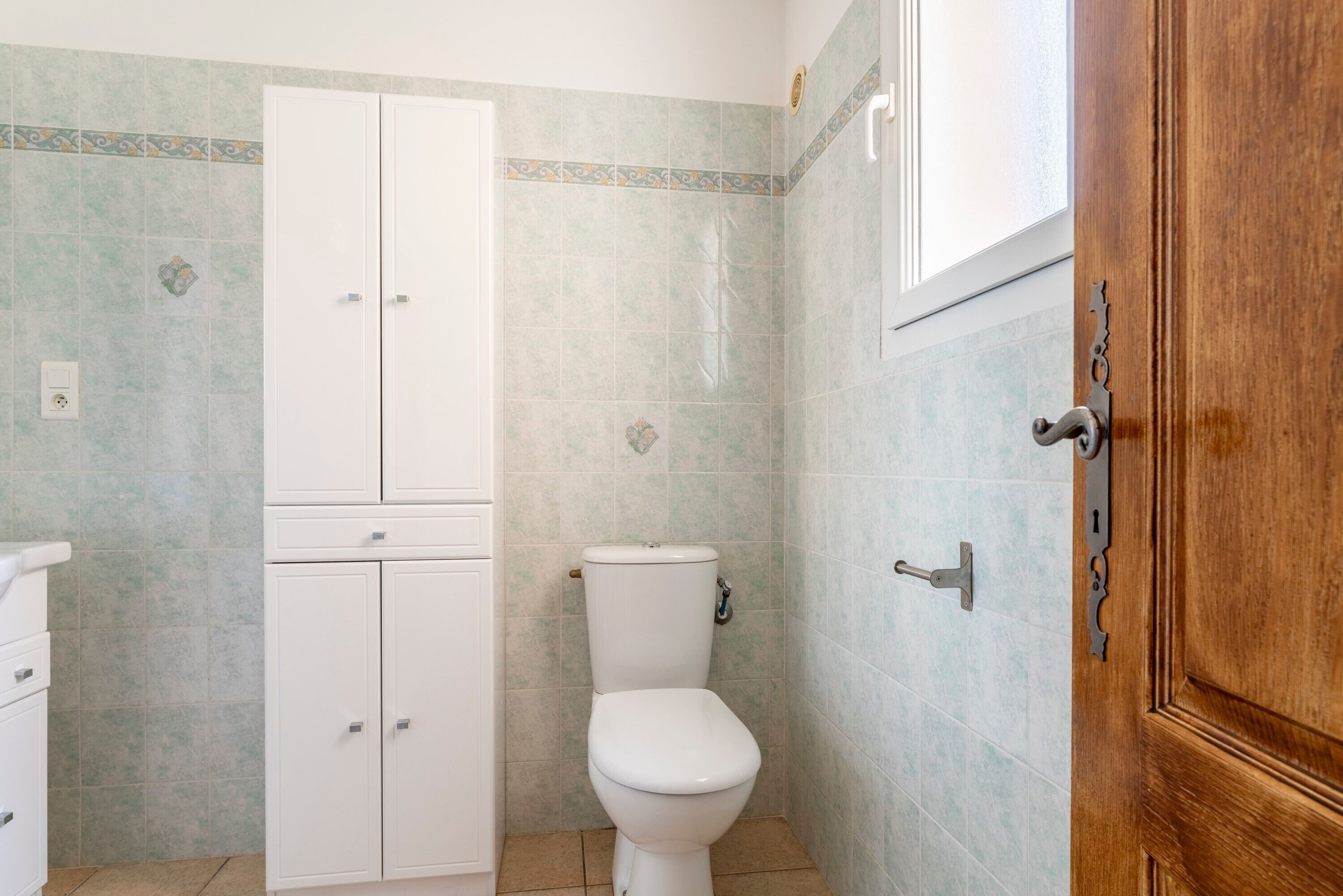 A bathroom with a toilet, a cabinet, and a wooden door.