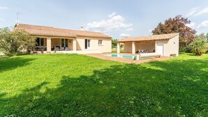 Ein zweistöckiges Haus mit Swimmingpool, überdachter Terrasse und gepflegtem Rasen.