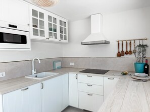 Una cocina moderna con armarios blancos, microondas integrado, campana extractora de acero inoxidable, un fregadero y utensilios de madera colgados en la pared.