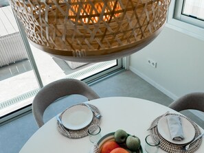 Un comedor con una mesa redonda, dos sillas, una cesta tejida colgando del techo y un cuenco con fruta.