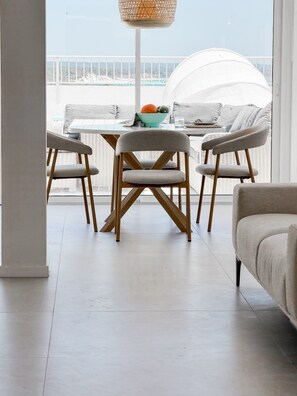 Una sala de estar moderna con vistas al balcón, que incluye una mesa de comedor con sillas, un sofá y una lámpara colgante.