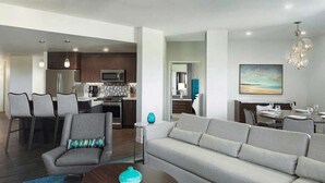 A modern living room with a sofa, armchair, and coffee table, a kitchen area with appliances, and a dining area with chairs. - Carlsbad | Comfortable Beach Stay | Pool + Ocean | 2BR Plus (Carlsbad)