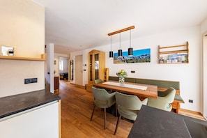 Cocina moderna con encimera de madera, zona de comedor con mesa y sillas de madera, y lámpara de pared.