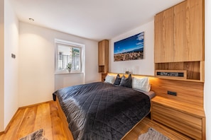 Un dormitorio con cama, cabecera de madera, ventana con vistas y un cuadro en la pared.
