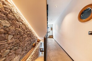 Un pasillo con pared de piedra, un banco de madera, un espejo y una escalera.