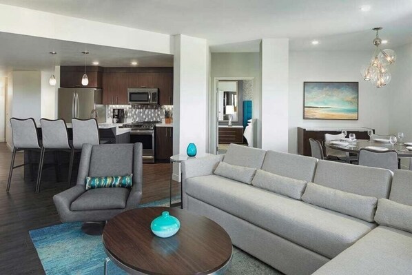 A modern living room with a sofa, armchair, and coffee table, a kitchen area with appliances, and a dining area with chairs.