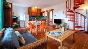 Een woonkamer met een bank, een salontafel en een televisie. Er is een keuken met houten kasten en een rode spiraaltrap.