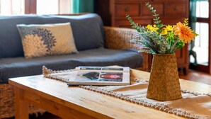 Een houten tafel met een gevlochten vaas met bloemen, een tijdschrift en een placemat in een kamer met een bank en een houten kast op de achtergrond.