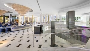 A spacious lobby with a central staircase, a modern chandelier, and a glass railing overlooking the lower level. - Direct Ocean View Studio at Sorrento Fontainebleau, Miami Beach (Miami Beach)