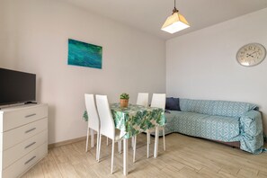 A dining area with a table, chairs, a sofa, a clock, and a television.