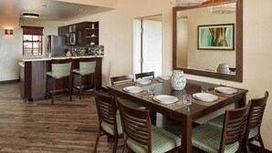 A dining area with a wooden table set for four, surrounded by chairs with striped cushions. A large mirror hangs above the table, reflecting part of the room.