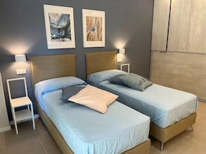 Une chambre avec deux lits, une table de chevet, une lampe fixée au mur et des œuvres d’art.