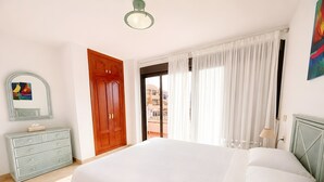 Un dormitorio con cama, cómoda, puerta y ventana con cortinas.