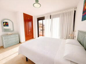 A bedroom with a bed, a dresser, a door, and a window with curtains.