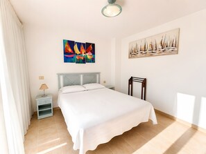 A bedroom with a bed, a nightstand, a lamp, a chair, and two paintings on the wall.