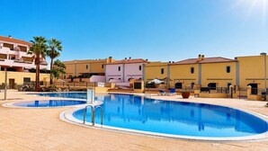 Zona de piscina con cielo despejado, palmeras y edificios con balcones.