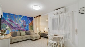 A living room with a sofa, a dining table with chairs, a large painting on the wall, and an air conditioning unit. - Apartment 'La Casa De Utiaca 28' with Wi-Fi (Las Palmas de Gran Canaria)