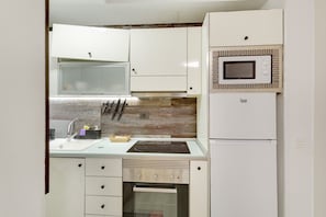 A compact kitchen with white cabinets, a microwave, a built-in oven, and a sink.