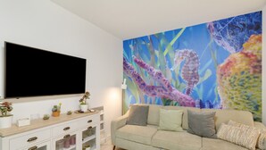 A living room with a flat-screen TV, a beige sofa, a white cabinet, and a colorful seahorse mural on the wall. - Apartment 'La Casa De Utiaca 28' with Wi-Fi (Las Palmas de Gran Canaria)