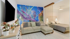 A living room with a sectional sofa, a bed, a TV, and a large seahorse mural. - Apartment 'La Casa De Utiaca 28' with Wi-Fi (Las Palmas de Gran Canaria)