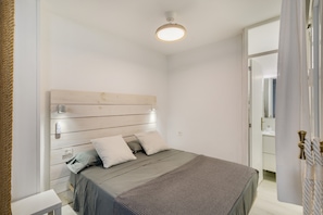 A bedroom with a wooden headboard, a bed with grey bedding, a bedside table, and a white wall.