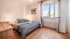 Een slaapkamer met een houten bed, een nachtkastje, een hanglamp, een wereldkaart aan de muur en een groot raam met gordijnen.