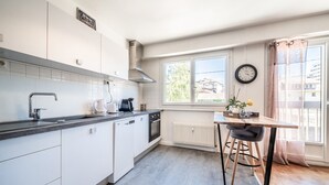 Een moderne keuken met witte kasten, een roestvrijstalen spoelbak, een inbouwoven en een raam met uitzicht op gebouwen.