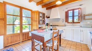 A kitchen with wooden cabinets, a dining table with chairs, a window with blinds, and a hanging light fixture. - Rural House 'Faustina' with Private Pool, Private Terrace, and Wi-Fi (Selva)