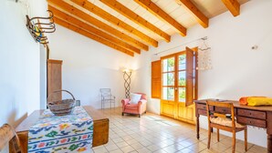 A room with a wooden ceiling, a tiled floor, a table with a patterned tablecloth, a pink chair, a wooden desk, and a window with a view of greenery. - Rural House 'Faustina' with Private Pool, Private Terrace, and Wi-Fi (Selva)