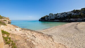 A coastal beach with clear turquoise water, rocky terrain, and a cliff with sparse vegetation. - Holiday Home 'Casa Noa' with Private Pool, Wi-Fi and Air Conditioning (Romàntica)