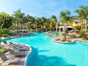 A large, clear swimming pool with multiple sunbathing areas and palm trees. - Carlsbad | Bright Beach Retreat | Pool + Ocean (Carlsbad)