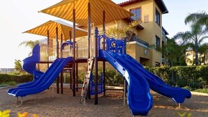 A playground with two blue slides and a yellow umbrella structure. - Carlsbad | Coastal Stay Made Easy | Pool + Ocean (Carlsbad)