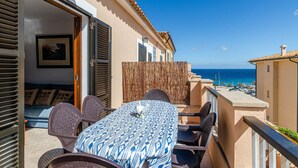 A balcony with a table and chairs, a view of the sea, and a building with a tiled roof. - YourHouse Sol i Mar 1 (Cala Mesquida)