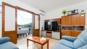 A living room with a sofa, a coffee table, a TV, and a kitchen area with cabinets and a TV. - YourHouse Sol i Mar 1 (Cala Mesquida)
