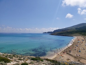 A beach with clear blue water, sandy shore, and a hilly landscape in the background.