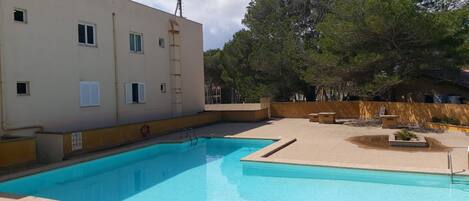 A swimming pool with a clear blue water, surrounded by a beige building with windows and a lifebuoy.