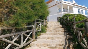 Una escala de pedra que mena a un edifici blanc amb balcons, envoltat de vegetació.