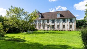 Un'ampia casa a due piani con un prato curato e un'area giardino con sedie in metallo.