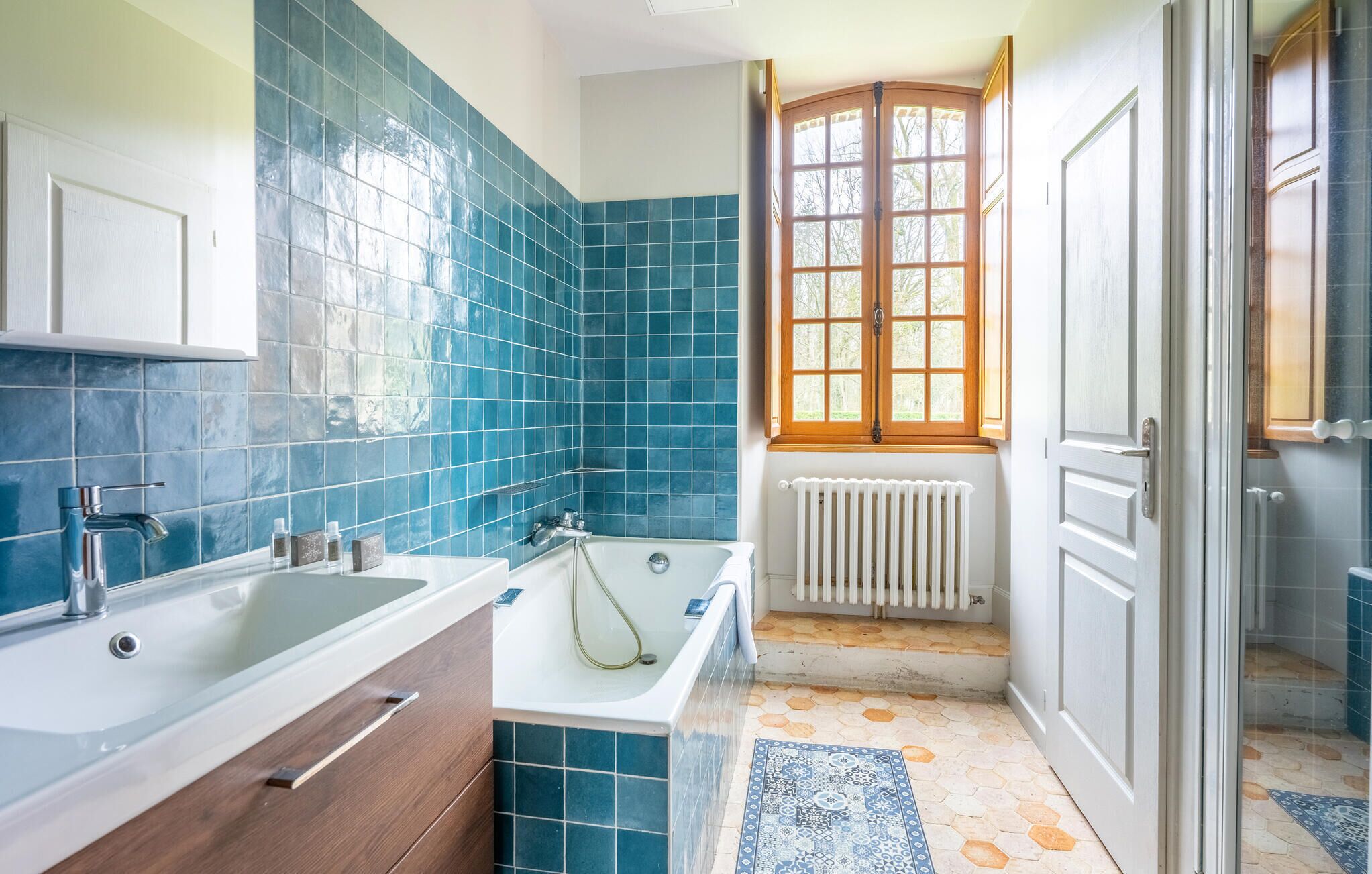 Een badkamer met een bad, een wastafel en een raam met uitzicht op bomen.