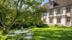 Una casa tradizionale con giardino, un tavolo in metallo bianco con sedie e un grande albero.