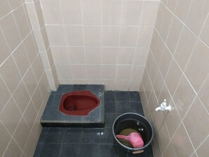A small bathroom with a red toilet, a black bucket, and a white faucet. - Wisma Sanggrahan (Bantul)