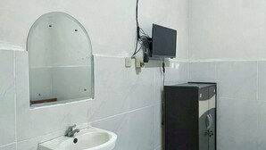 A bathroom with a white sink, a mirror, a black cabinet, and a wall-mounted television. - Wisma Sanggrahan (Bantul)
