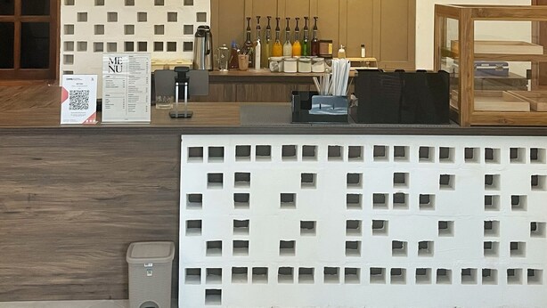 A reception area with a wooden counter, hanging pendant lights, a wall with a geometric pattern, and a tiled floor. - Wisma Sanggrahan (Bantul)