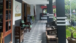 A covered outdoor seating area with patterned flooring, wooden furniture, and a potted plant. - Wisma Sanggrahan (Bantul)