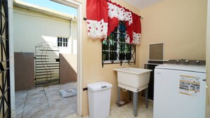 Une cuisine compacte équipée d’un lave-linge, d’un évier et d’une fenêtre agrémentée de rideaux décoratifs.