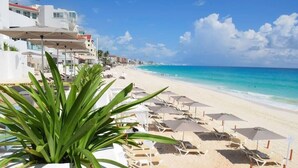 A beach with white buildings, a row of sun loungers under umbrellas, and a clear blue sky. - Brand new studio at the beach, gym, pool, jacuzzi, spa (Cancún)