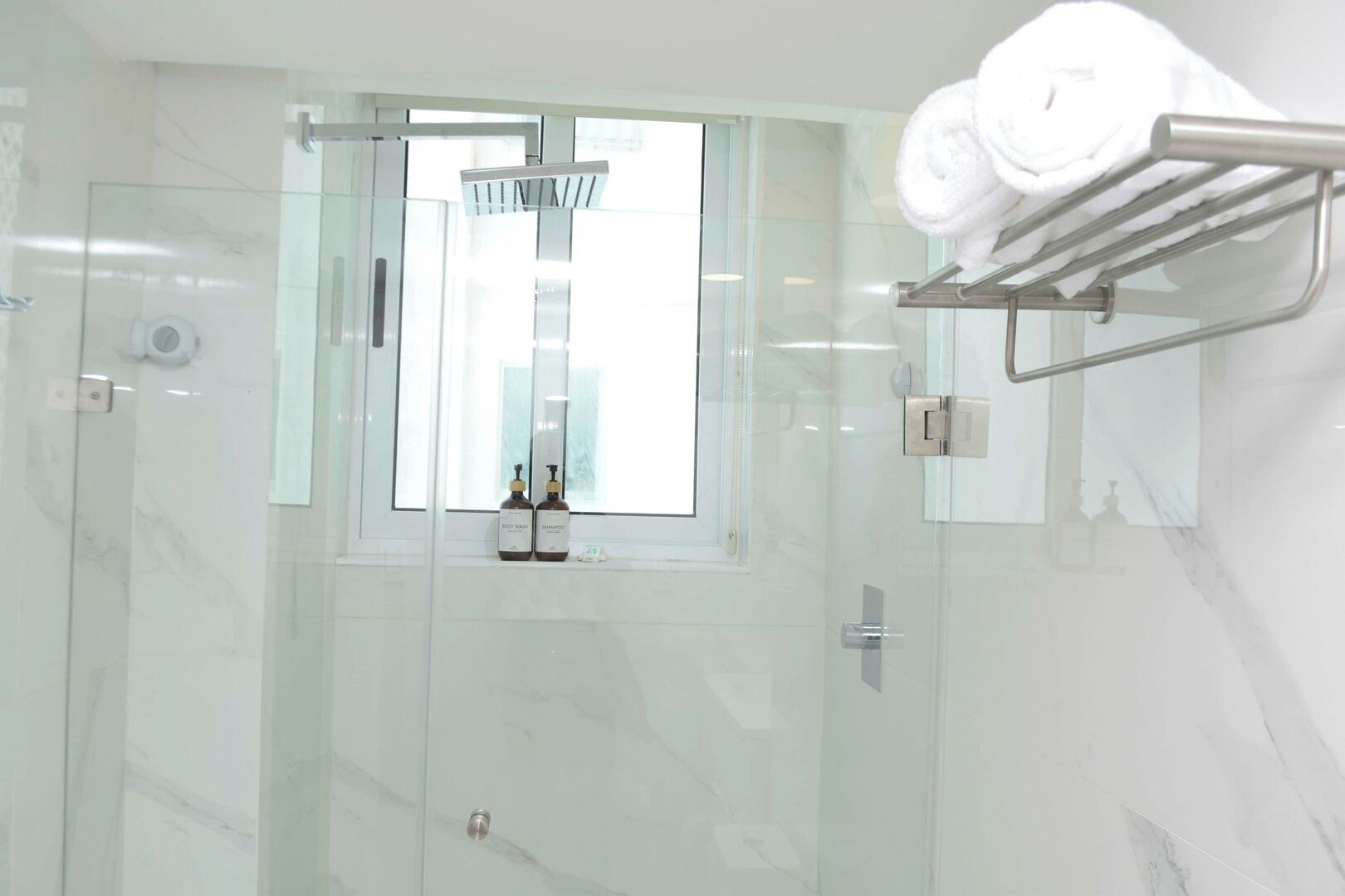 Ein modernes Badezimmer mit einer Duschkabine aus Glas, einem Handtuchhalter und einem Fenster mit Blick auf ein Gebäude.